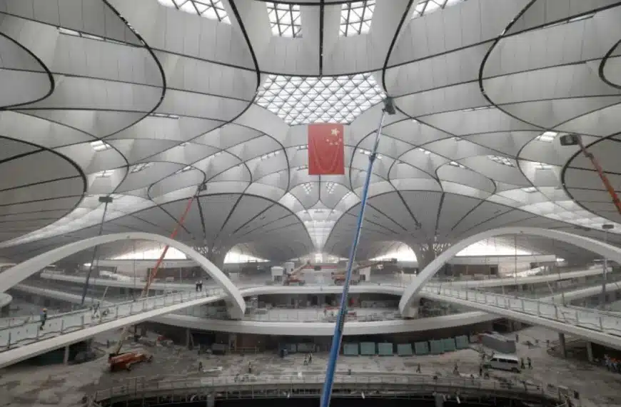 "Interior hall of Beijing Daxing Airport showcasing the steel grid roof structure with C-shaped columns and a Chinese flag hanging in the center."