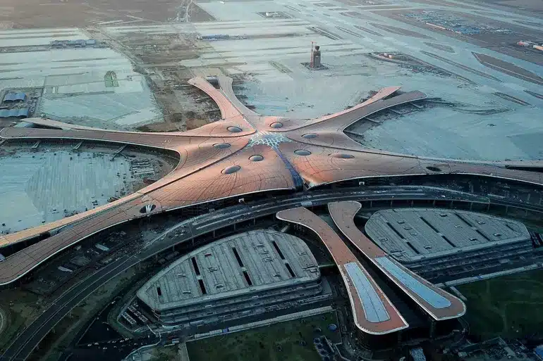 "Aerial view of Beijing Daxing Airport showcasing its radial design with extended wings, surrounded by runways and roads."