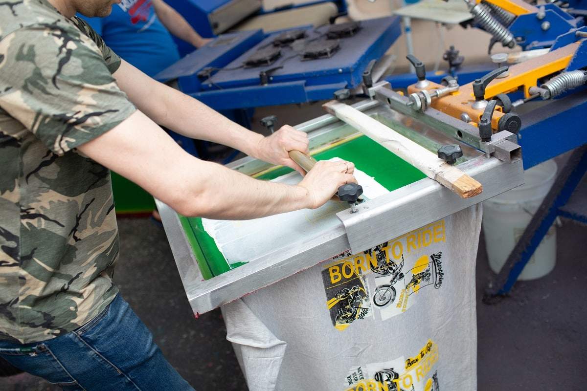 Serigraphy silk screen print process at clothes factory. Frame, squeegee and plastisol color paints. What is screen printing.