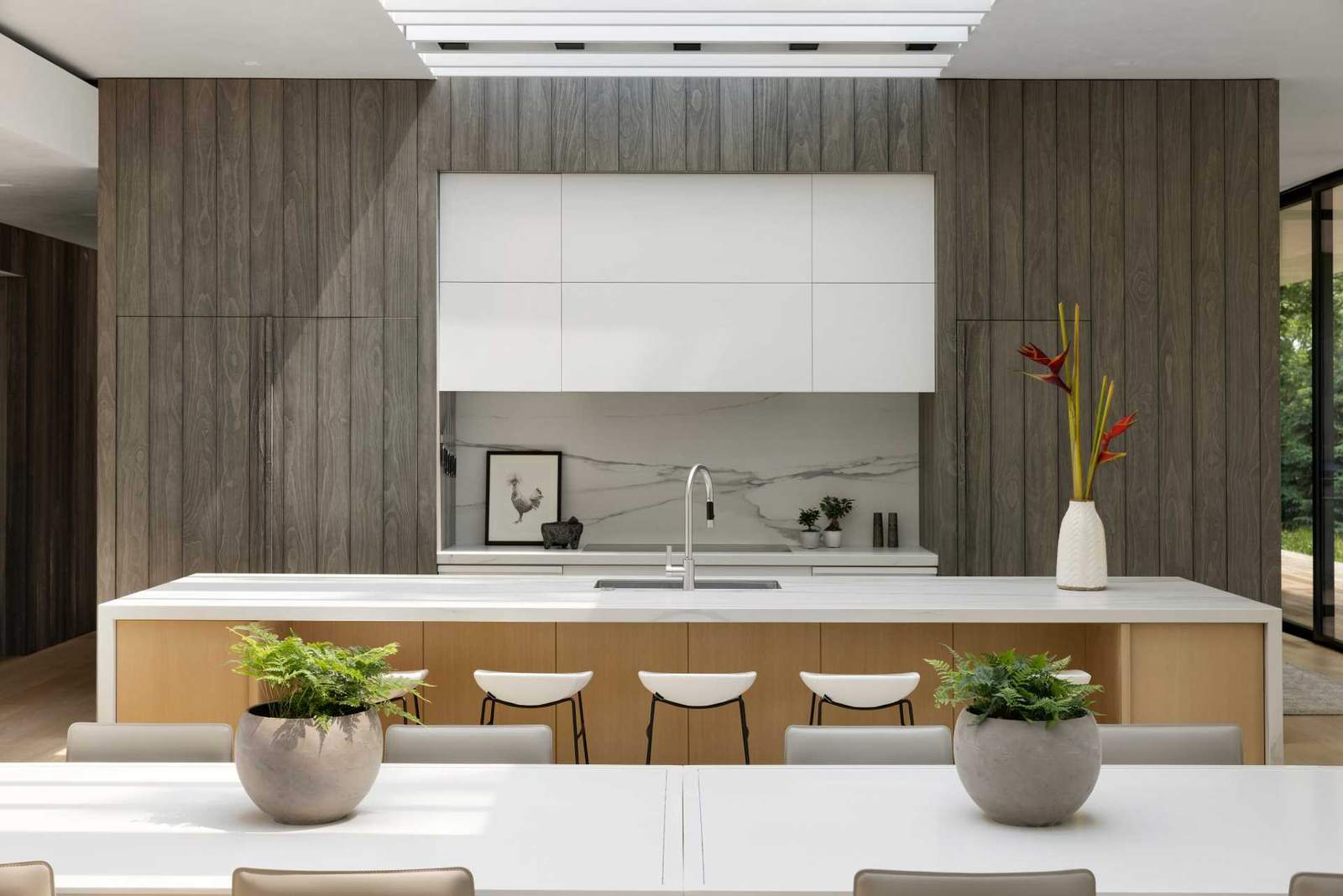 In this kitchen, a large island creates plenty of counter space, while an integrated fridge blends into the vertical wood accent.