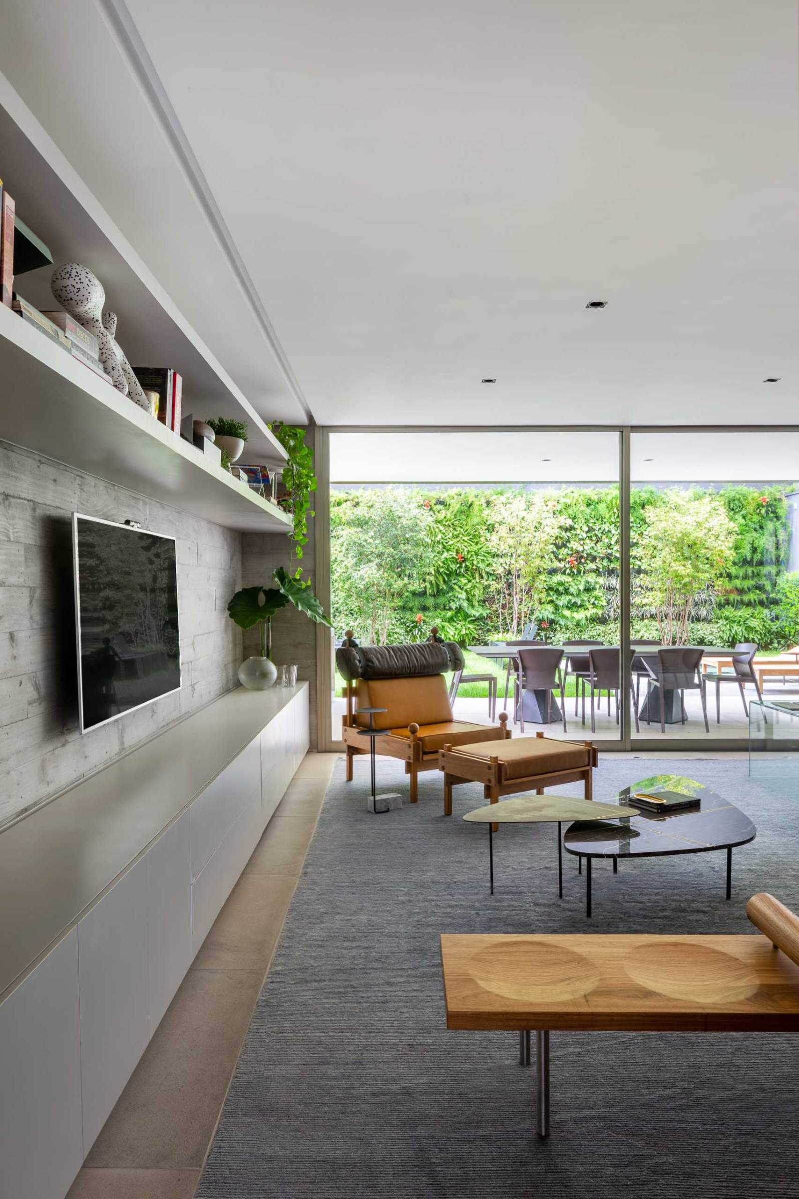 The furniture in this modern living room faces a concrete wall that been designed with a row of cabinetry below the TV and two shelves above.