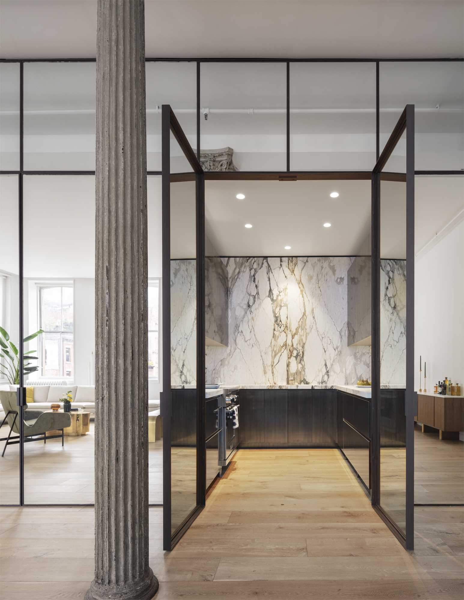A mirrored set of doors opens into the kitchen where matte figurative marble and patinated brass millwork play off of the loft’s new wide-plank oak floors.