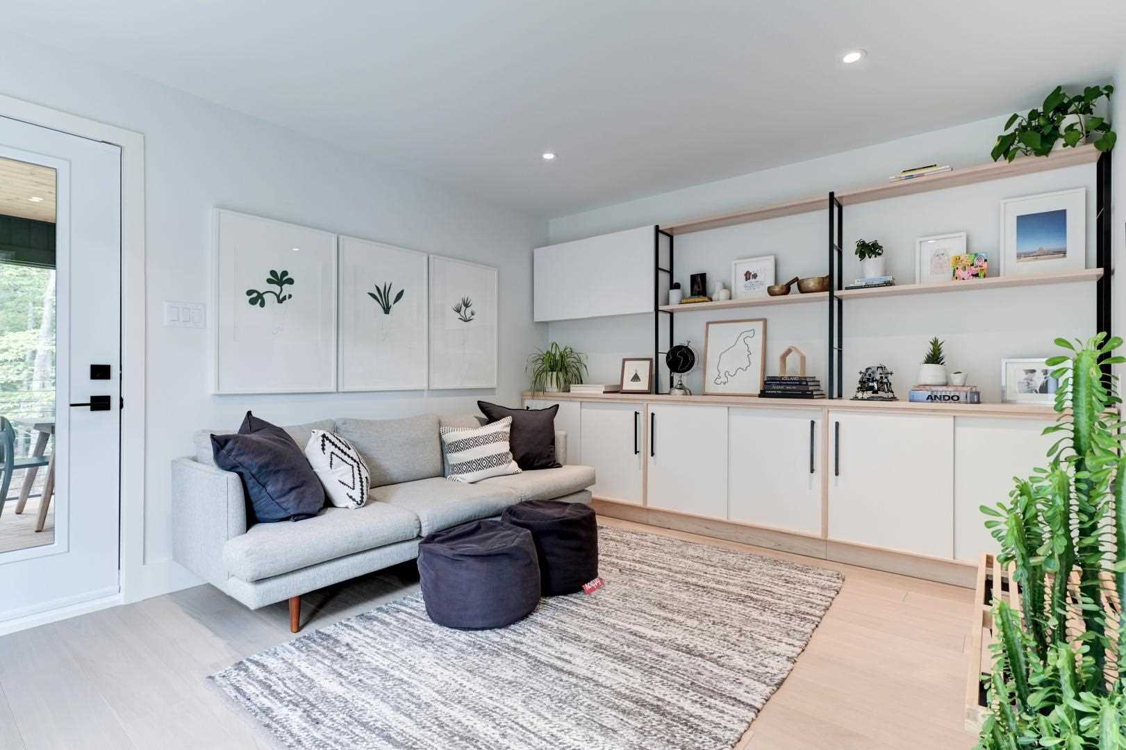 A living room includes a custom unit lines the wall with cabinets, and shelves accented by black elements and plants.