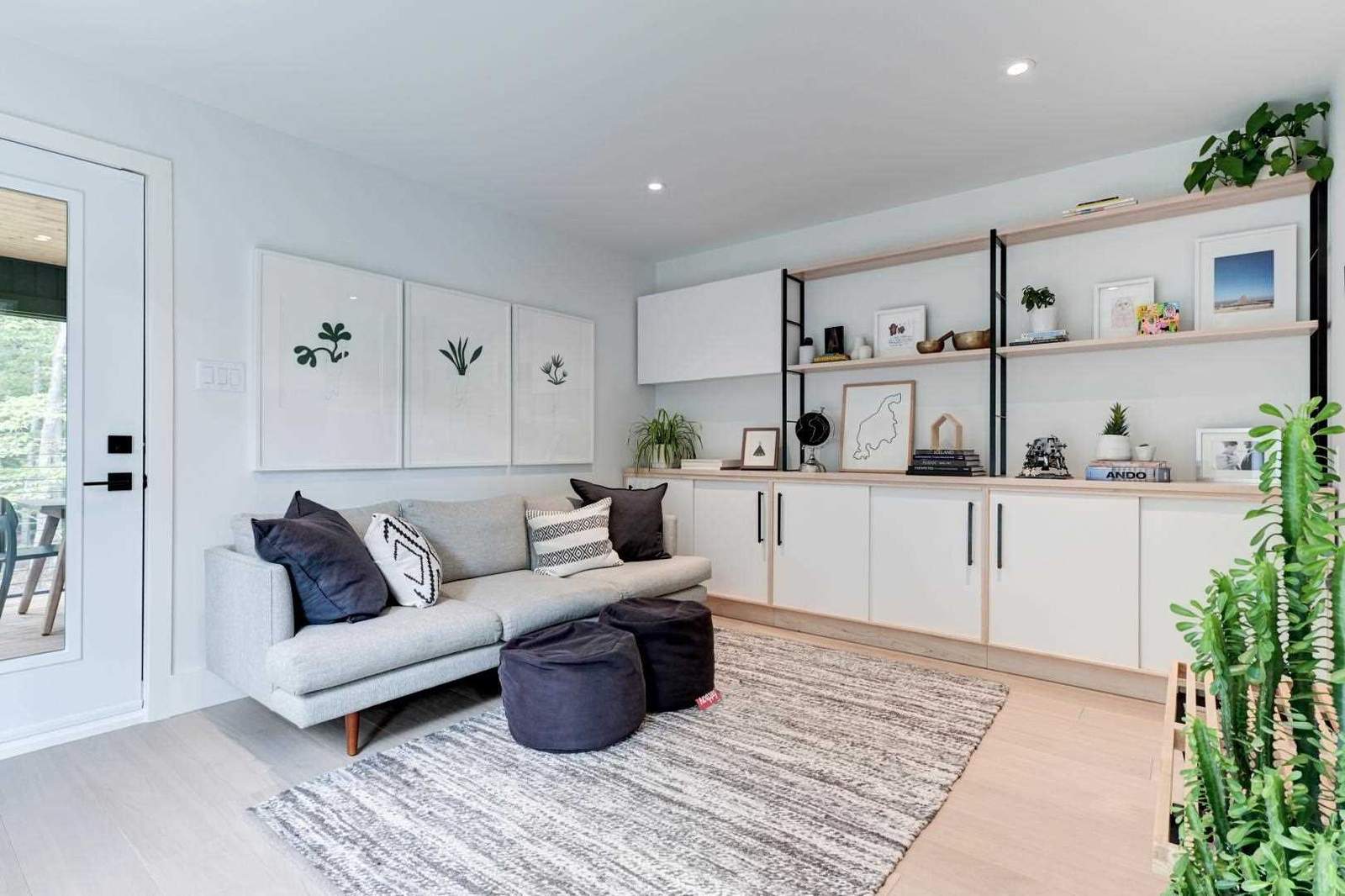 A living room includes a custom unit lines the wall with cabinets, and shelves accented by black elements and plants.