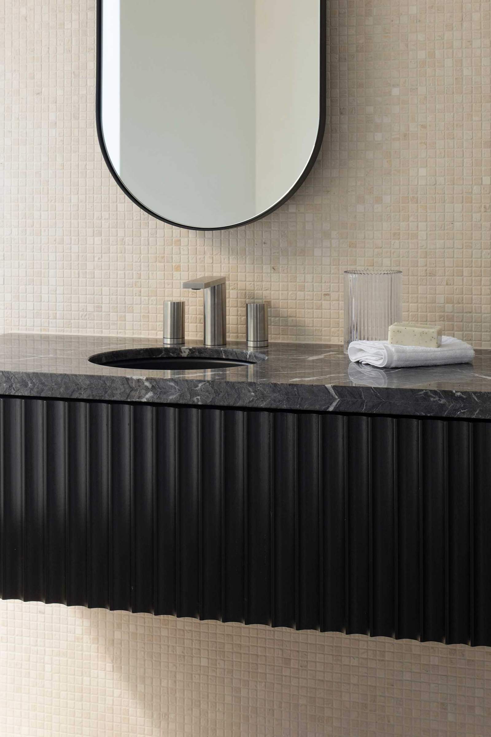 This modern bathroom is wrapped in a travertine mosaic tile providing a subtle textural quality to the space and contrasting with the solid floating vanity of stained timber and stone.