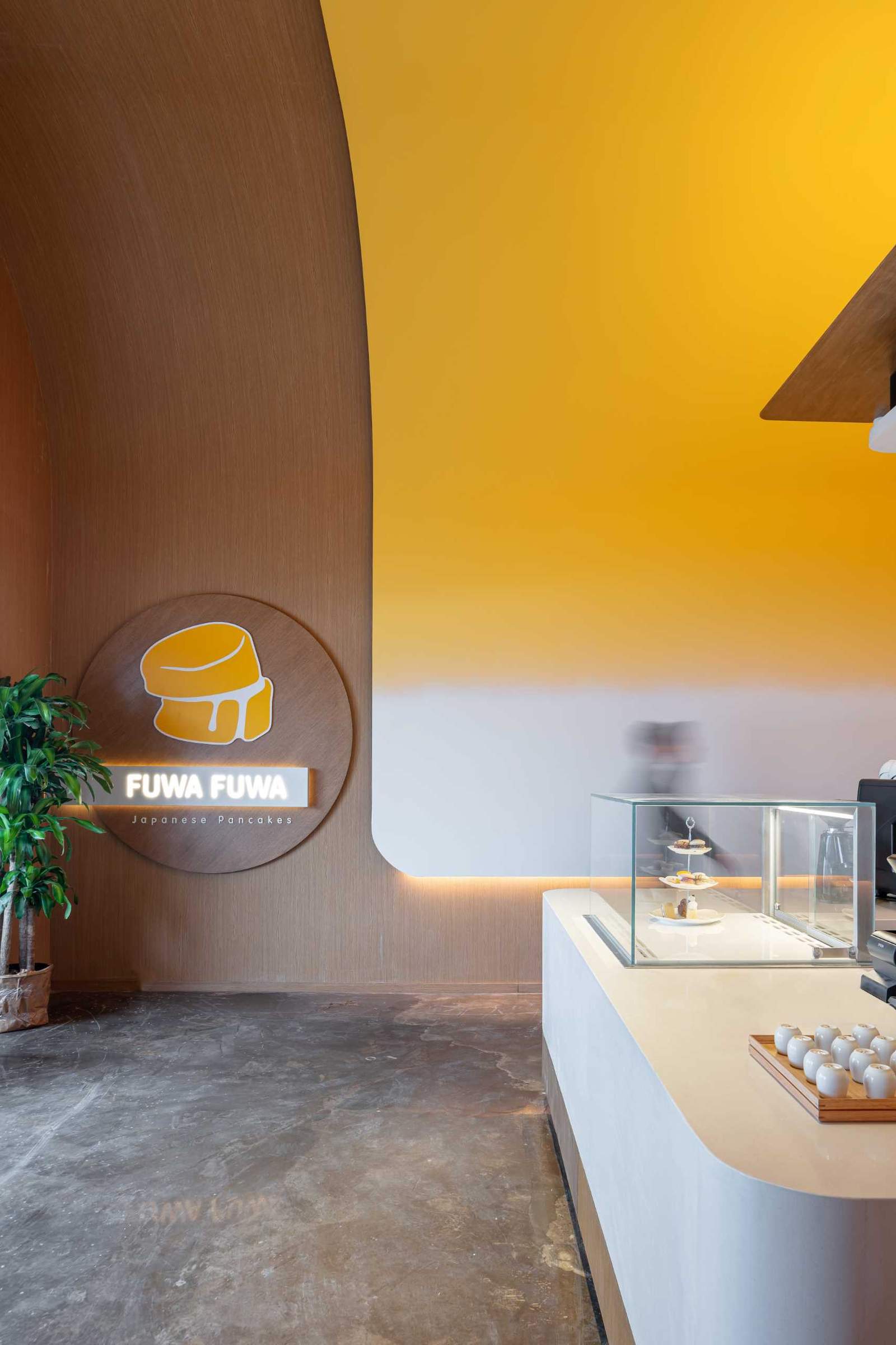 A modern cafe with hidden lighting and a curved yellow ceiling.