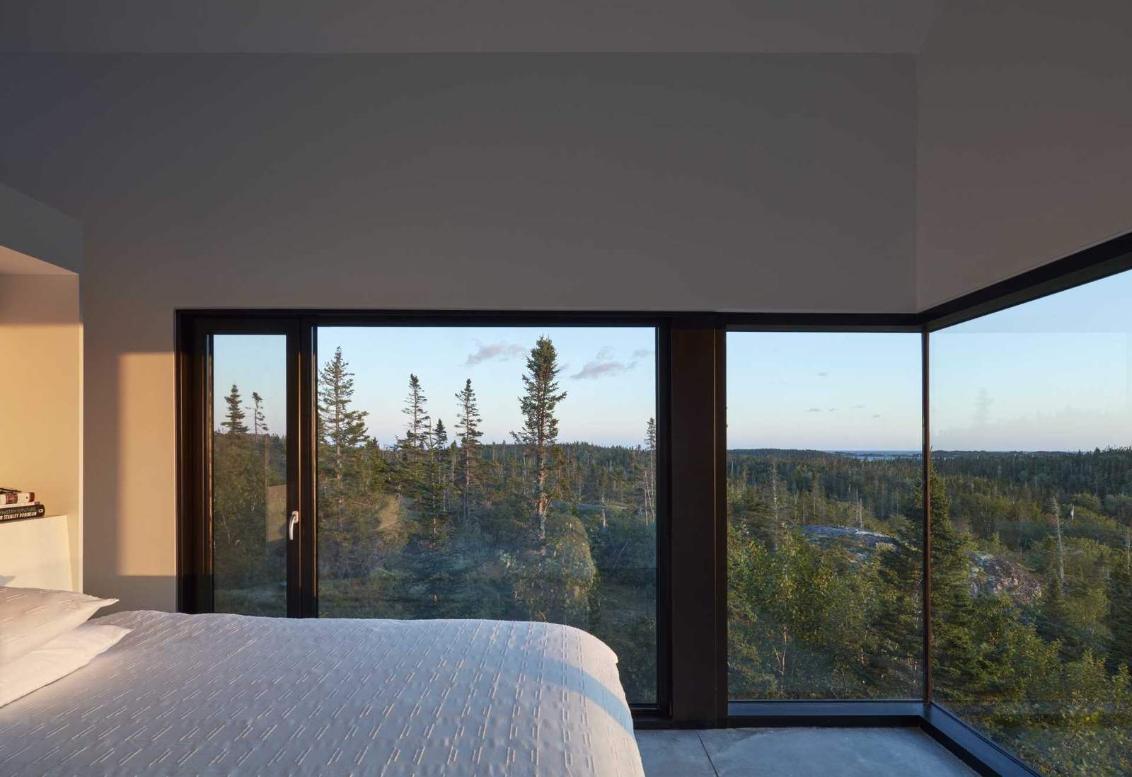 In this modern bedroom, the wrap-around black-framed windows showcase the uninterrupted view of the trees.