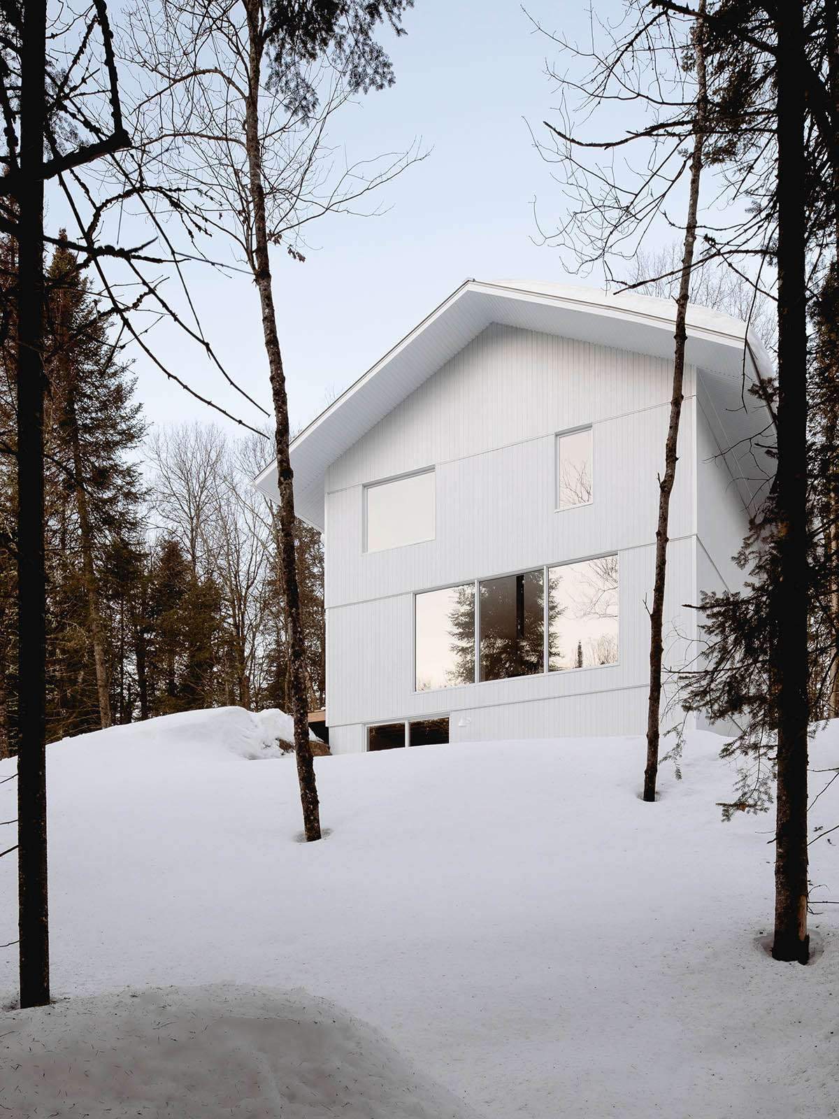 A Canadian winter house looks like it's covered in snow in the woods