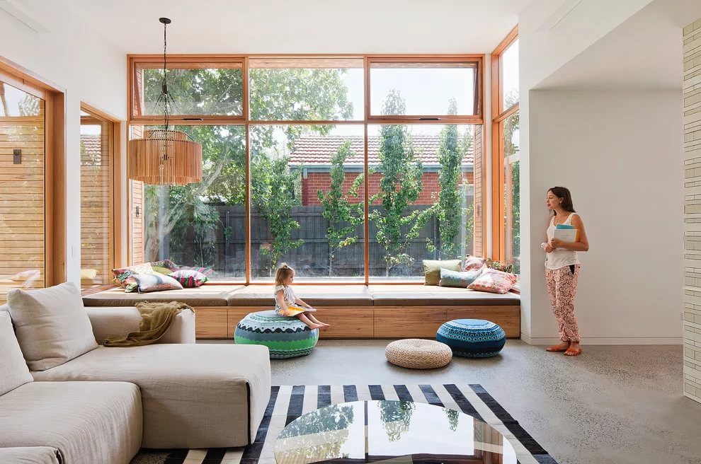 "Bright living room with tall windows allowing ample natural light, featuring a cozy seating area in front of the window."