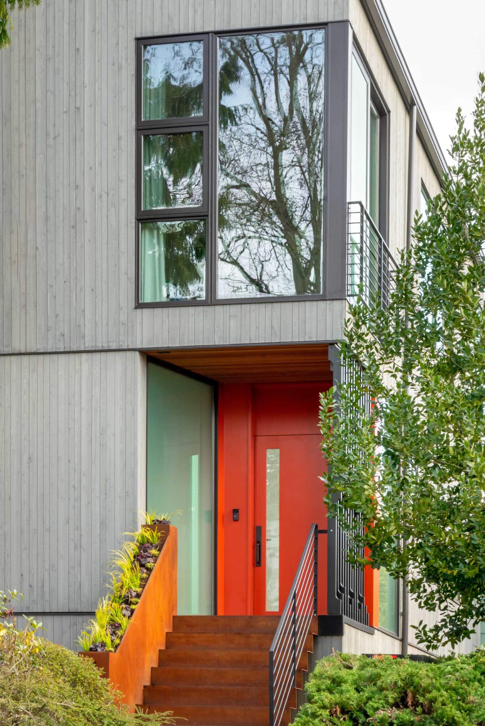 A modern house with a colorful front door, a steel planter, and a screen for added privacy.