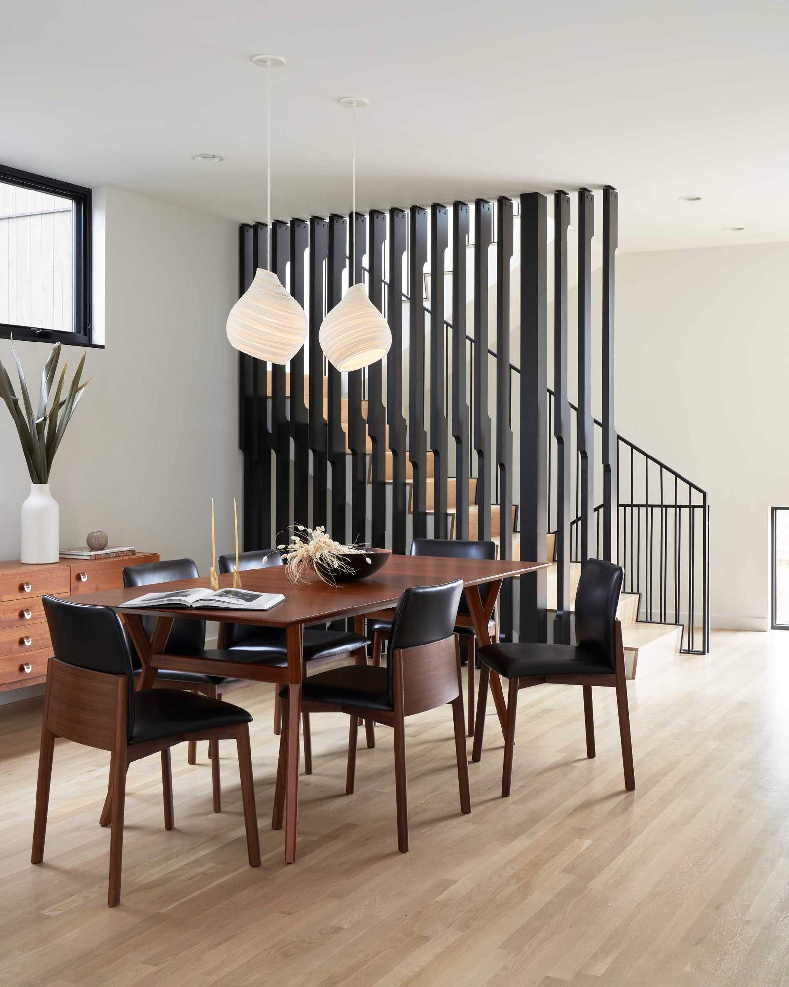 A modern dining room with a warm wood table and a pair of sculptural pendant lights.