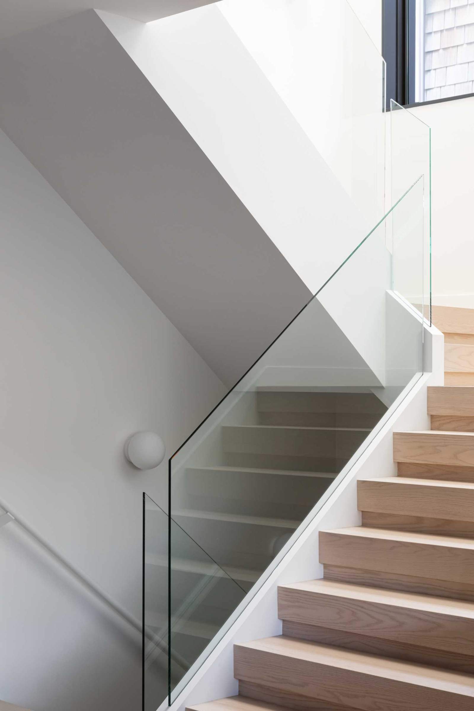 تربط السلالم الخشبية ذات الدرابزين الزجاجي المستويات المختلفة لهذا المنزل الحديث.