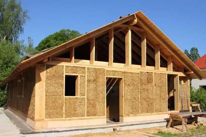 "A house under construction using sustainable building materials like wood and straw, showcasing an innovative eco-friendly design.
