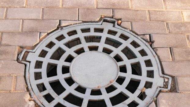 Cast-iron stormwater drainage hatch on the road before asphalt pavement. Drainage of rainwater from the road surface. Close-up. Conclusion