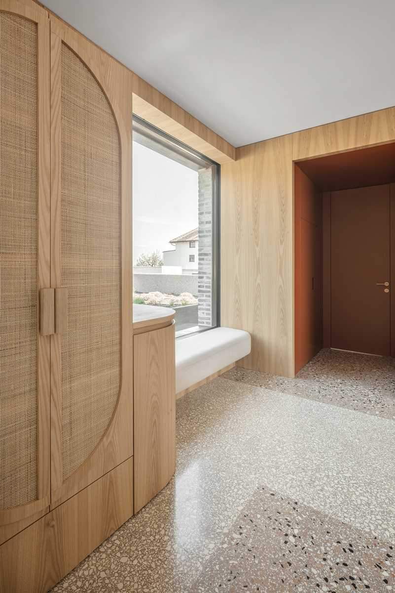 A wall of wood cabinets ends at a built-in bench underneath a window.