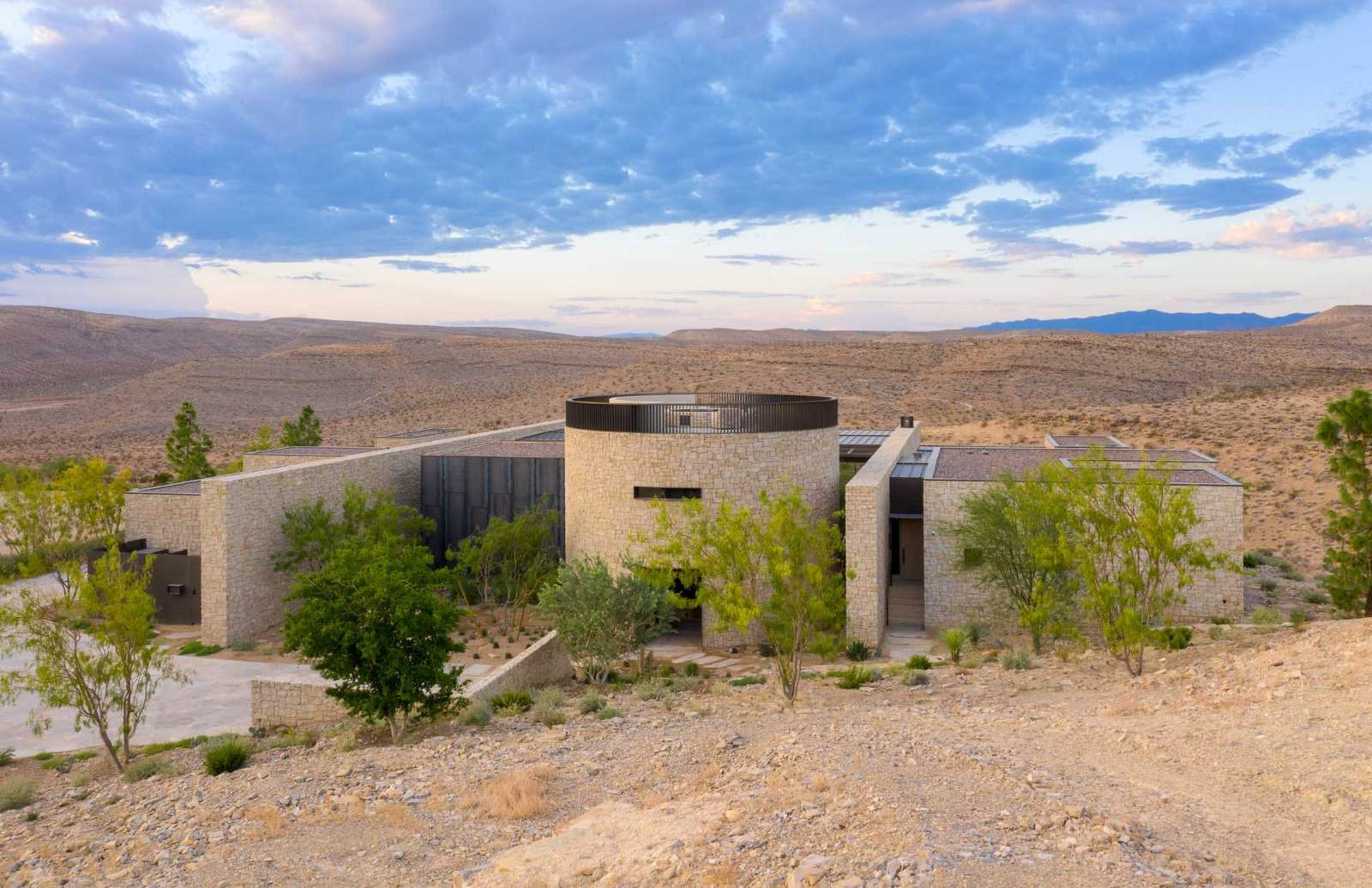 A modern home in the desert features weathered and hot rolled steel, stone walls, sliding glass panel walls, and travertine.