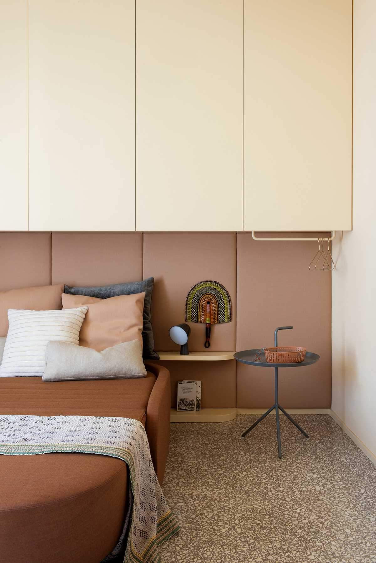 In this modern bedroom, an upholstered headboard lines the wall, while cabinets are located above the bed.