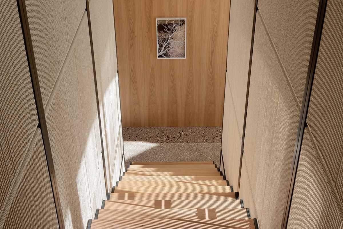 Modern wood stairs lead to a hallway with a wall of wood cabinets.