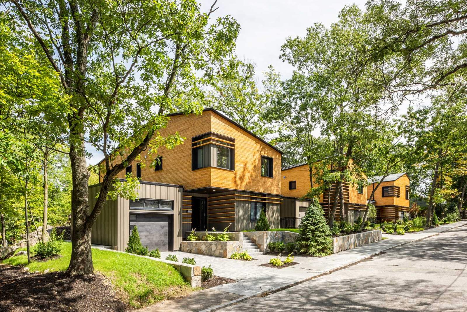 A collection of modern homes feature unique angled roof lines, a clear-finished white cedar siding on the upper volume, and a painted siding made from materials recovered from manufacturing by-products on the lower volume.