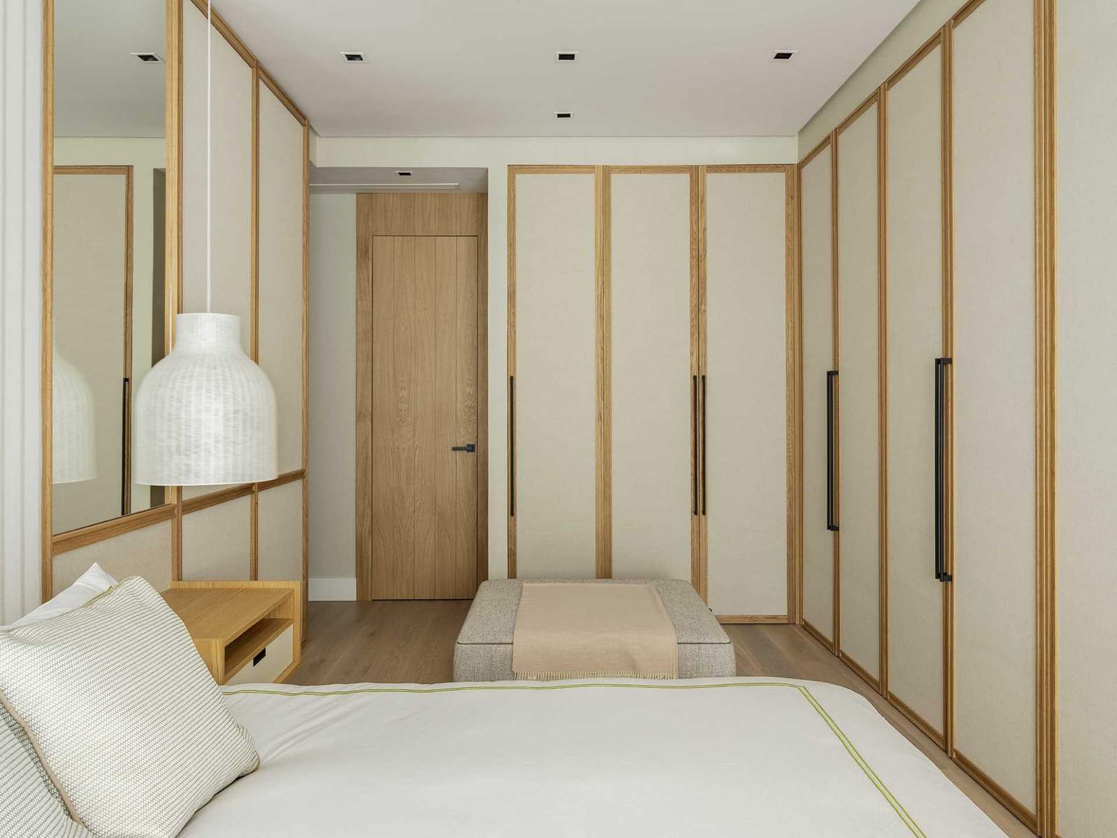 تزين الألواح القماشية والمرايا جدار غرفة النوم هذه، بينما تحتوي الطاولات الجانبية للسرير العائمة على أضواء معلقة معلقة فوقها.