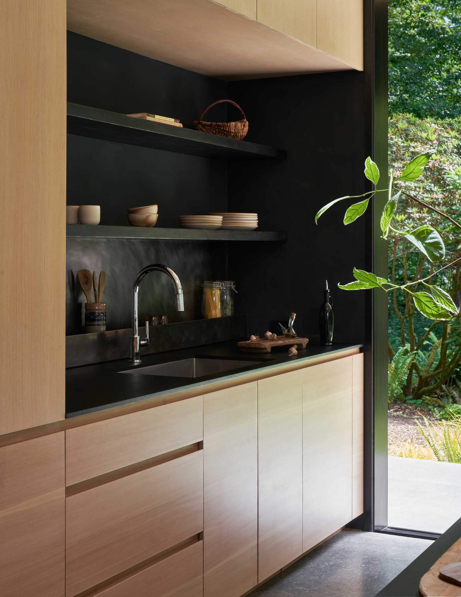 This modern kitchen features custom wood cabinets, dark countertops, and a custom blackened stainless steel backsplash.