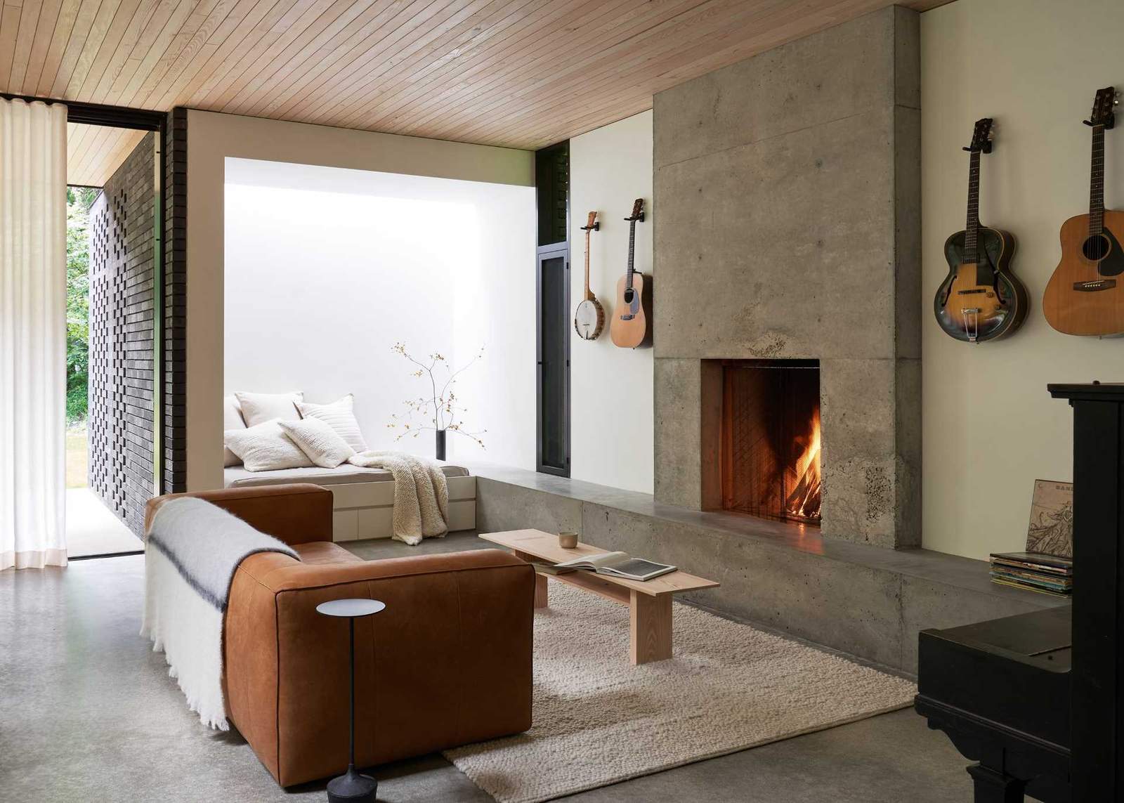 In this modern living room, the concrete hearth of the fireplace lines the wall and transitions into a bench with a skylight above.