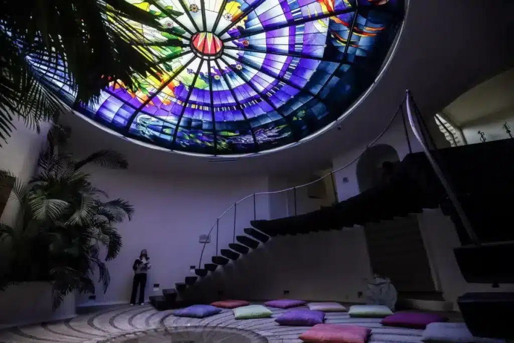 "Colorful glass skylight illuminating a meditation room with cushion seating and indoor plants."