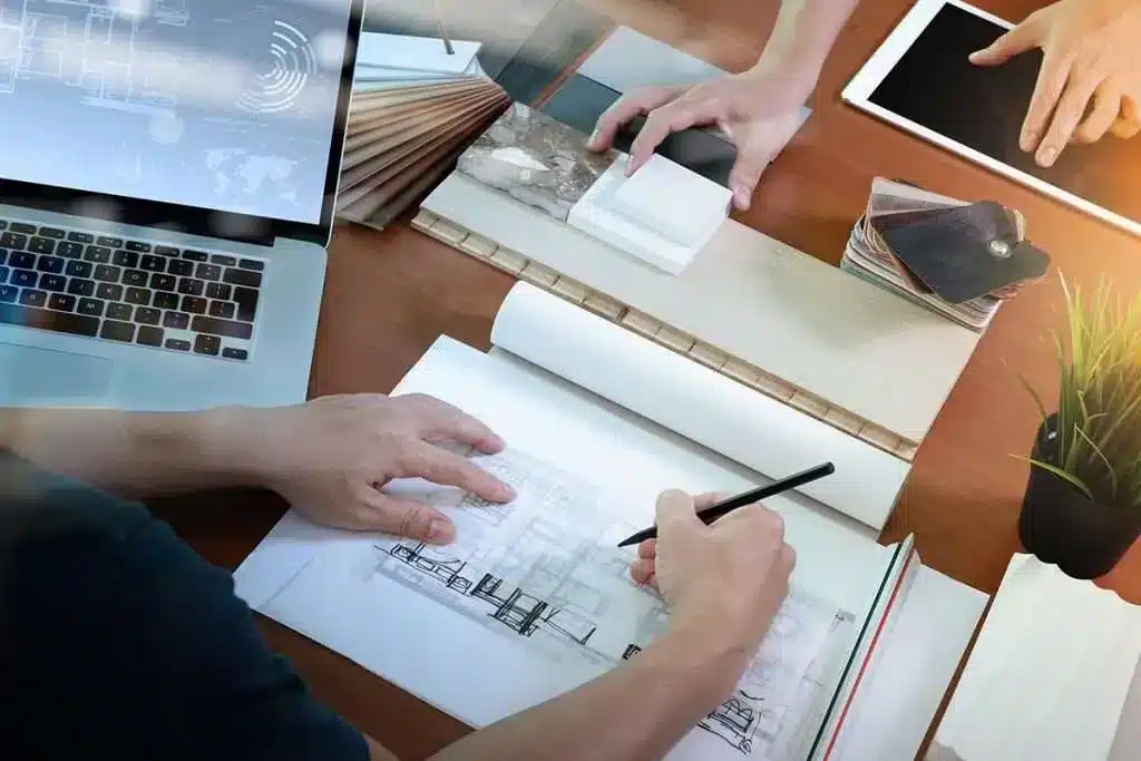 "An architect sketching a design on paper, using tools like a laptop and engineering plans."