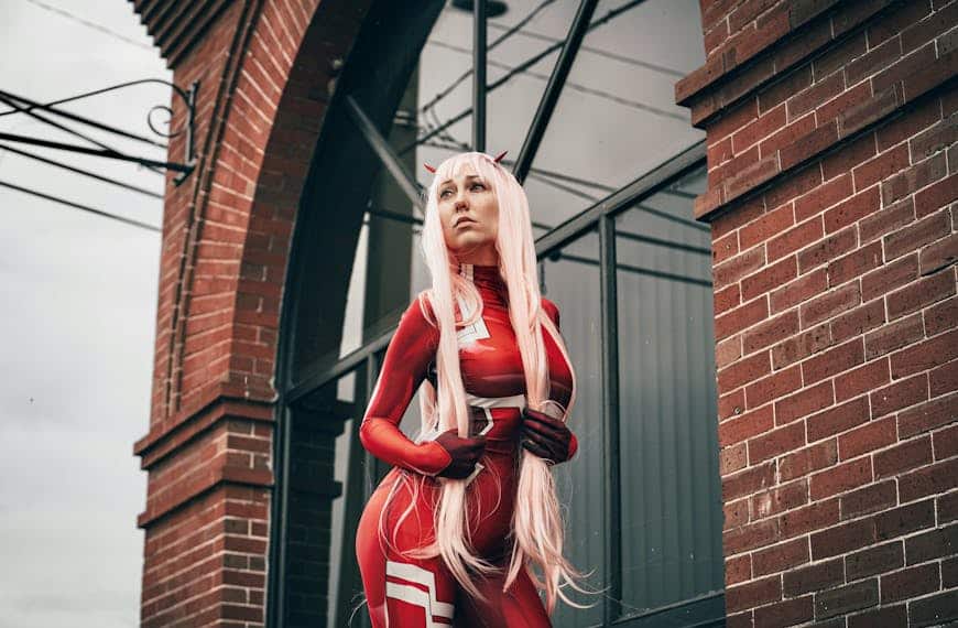 A cosplayer in a red costume poses confidently against a brick building.