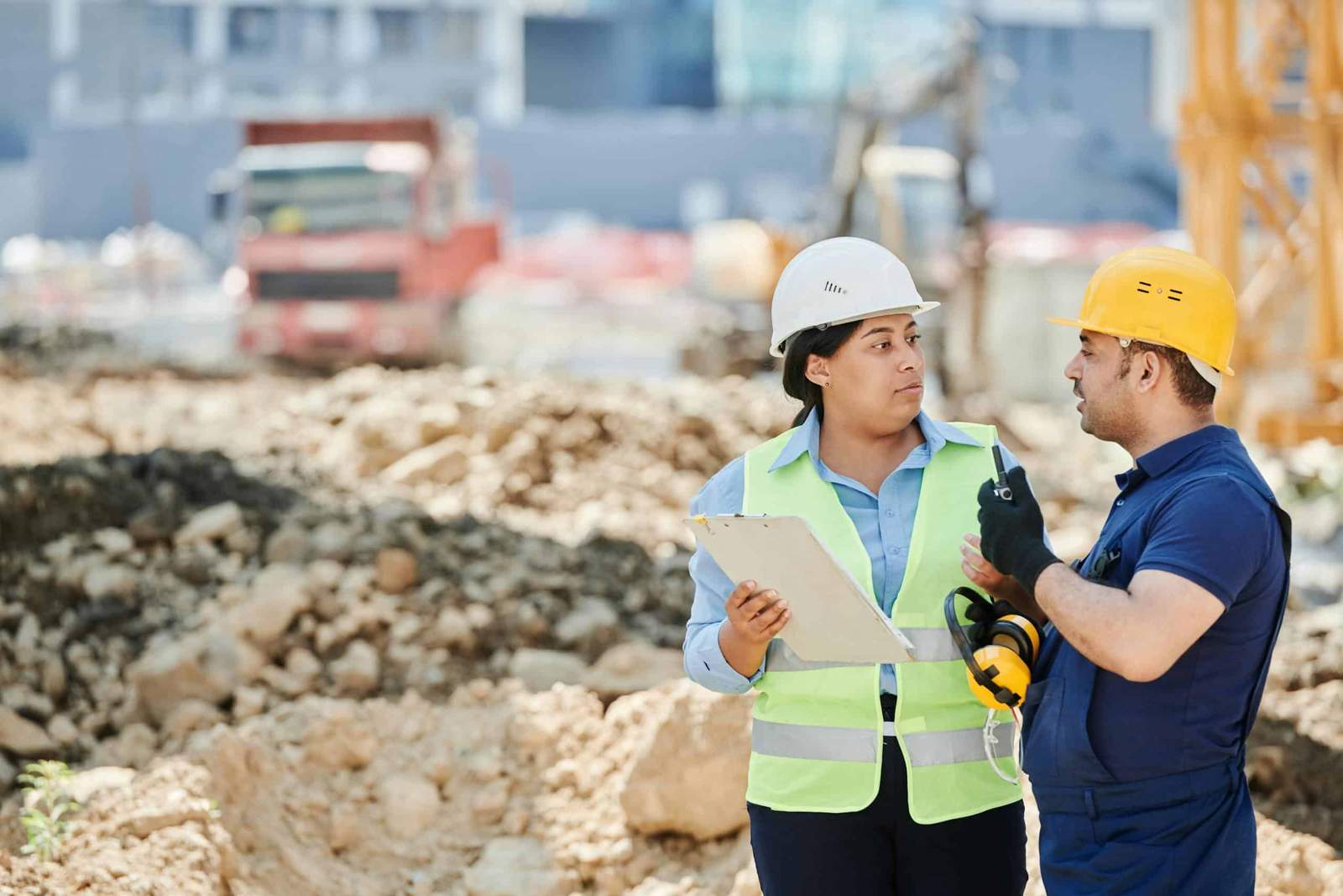 A Man and a Woman Wearing Hard Hats Talking at the Construction Site