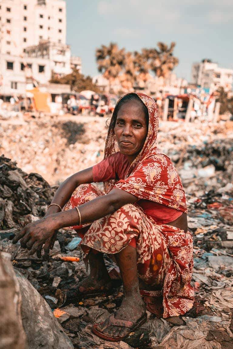 A woman in traditional attire sits at an urban dumpsite, highlighting waste challenges.