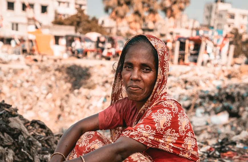 A woman in traditional attire sits at an urban dumpsite, highlighting waste challenges.