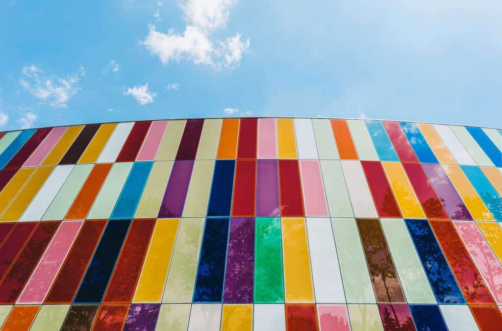 A colorful glass facade with vertical stripes under a bright blue sky, showcasing modern architecture.