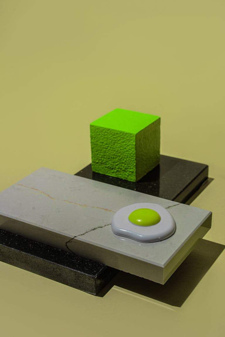 Artistic still life of a neon green cube and egg shape on geometric tiles. Modern and conceptual.