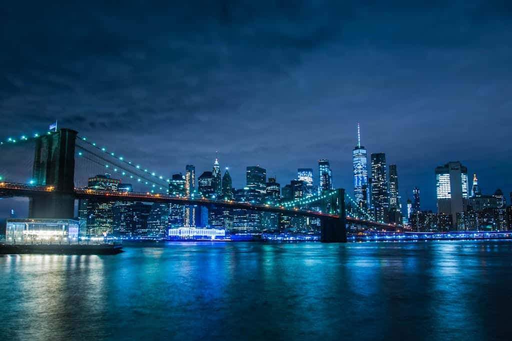 Stunning night view of the illuminated Brooklyn Bridge and New York City skyline across the water.