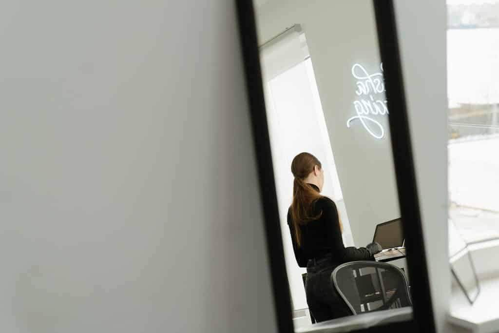 Woman working on a laptop in a sleek modern studio with a neon sign reflection.