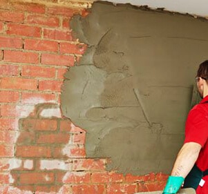 "A person working on infrastructure development by repairing a wall with cement, reflecting the importance of improvement in various fields."