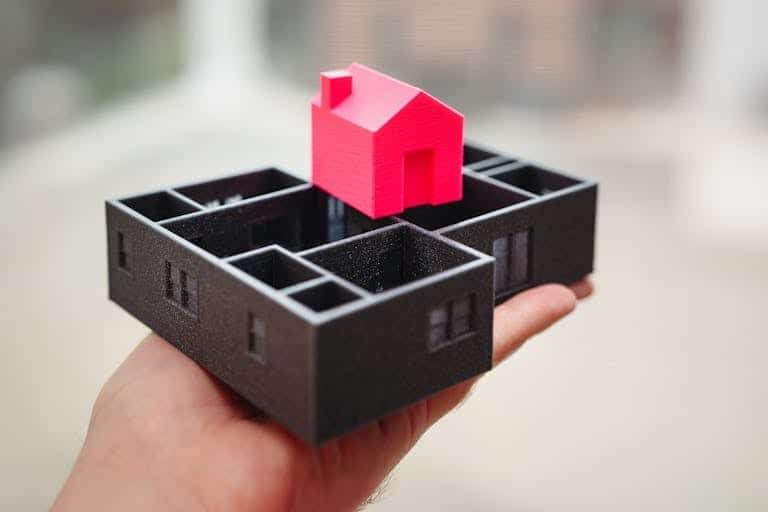 A hand holding a 3D printed model of a house and floor plan, showcasing architectural design.