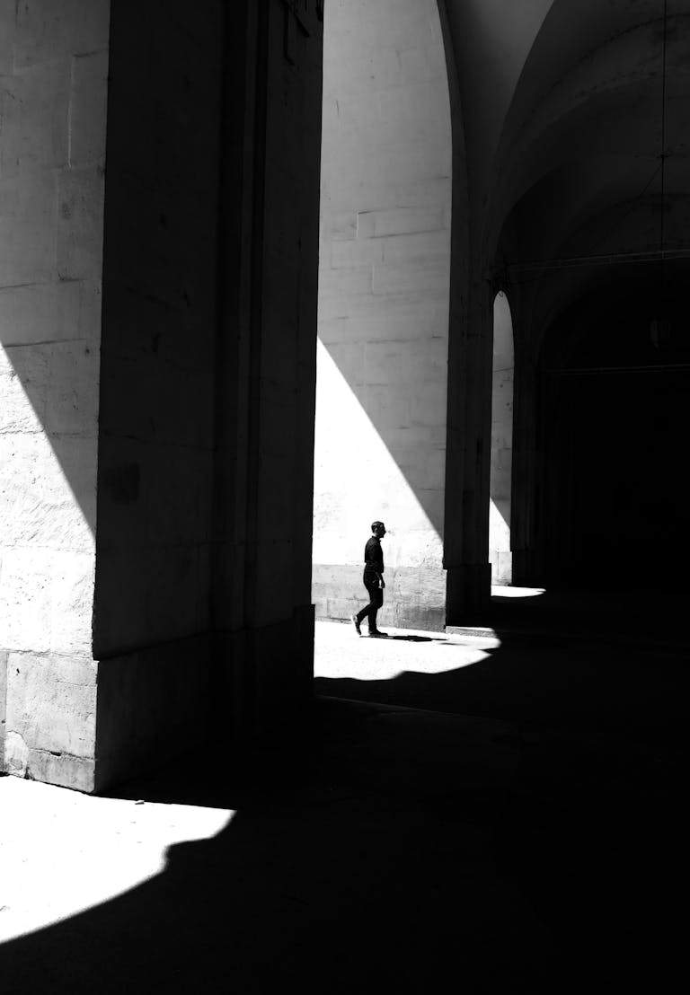 Dramatic black and white photo of a silhouette in a sunlit arched passage in Nancy, France.