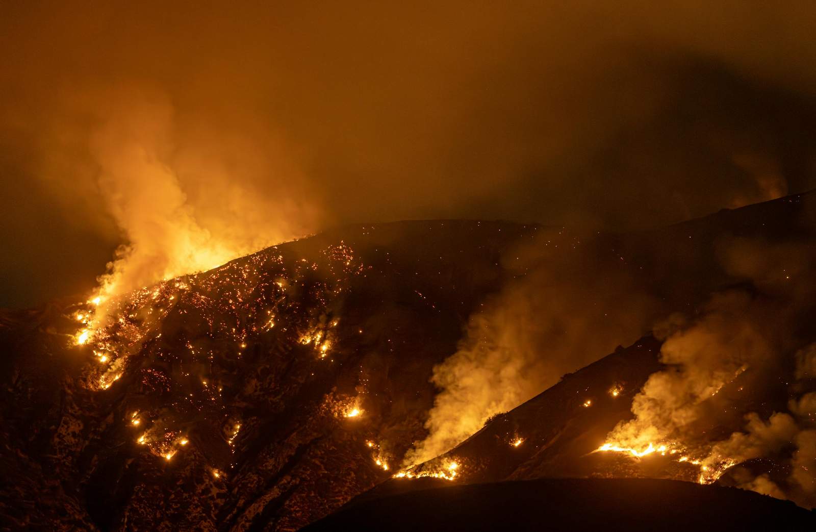 Intense wildfire blazing through mountains in California at night, creating a dramatic scene.