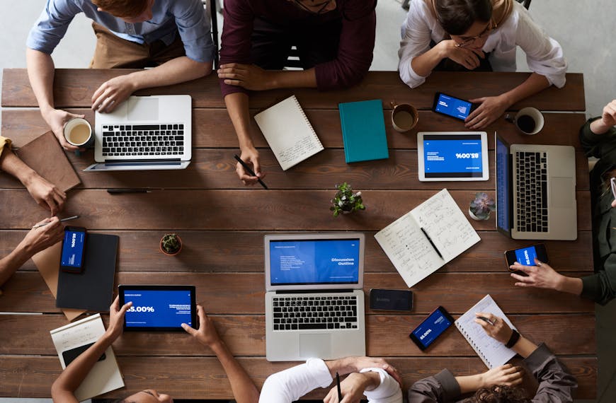 Overhead view of a diverse team in a business meeting using laptops and tablets.