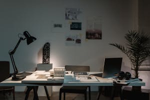 A contemporary architect's desk with design plans, laptop, and lamp in a spacious office.