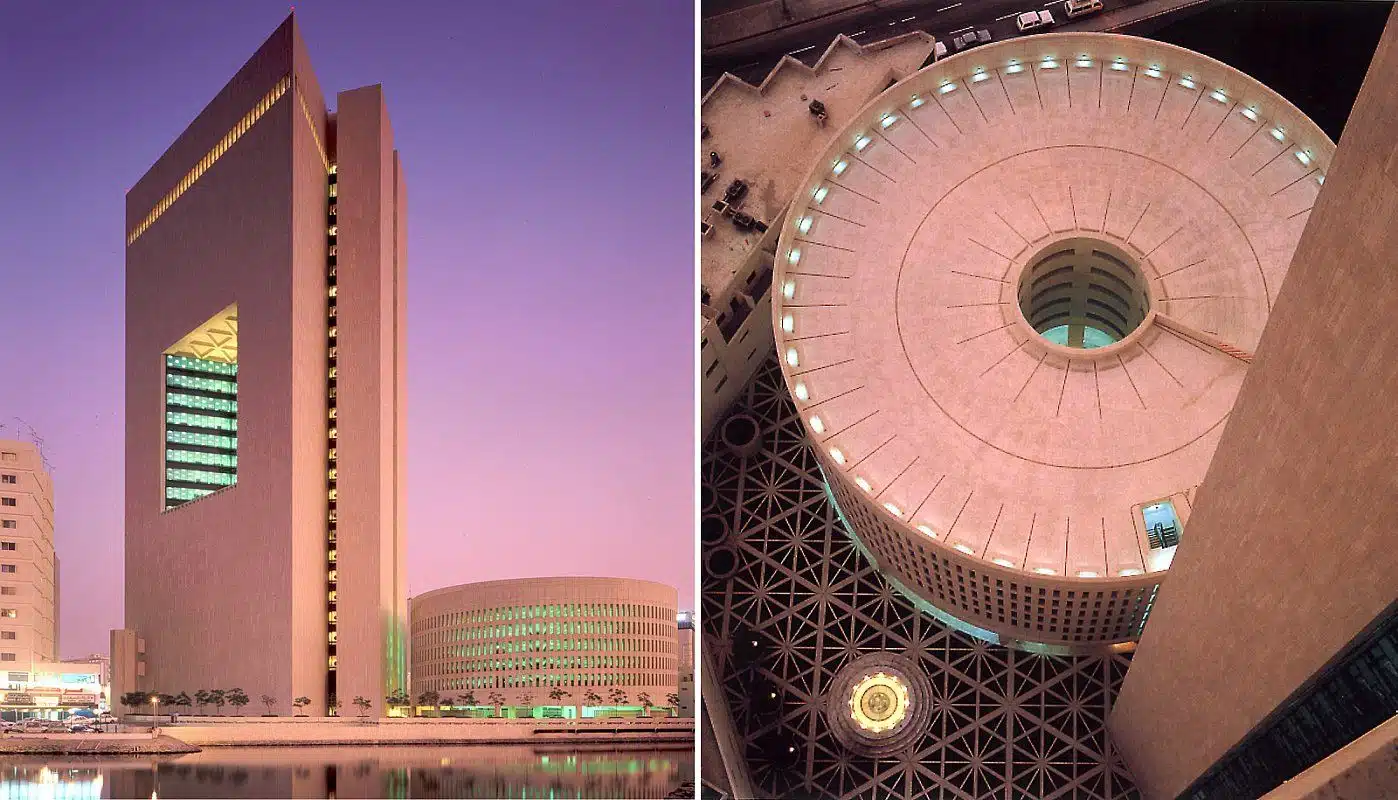 A tall modern building next to a circular structure, with an aerial view of the circular building's uniquely designed roof.