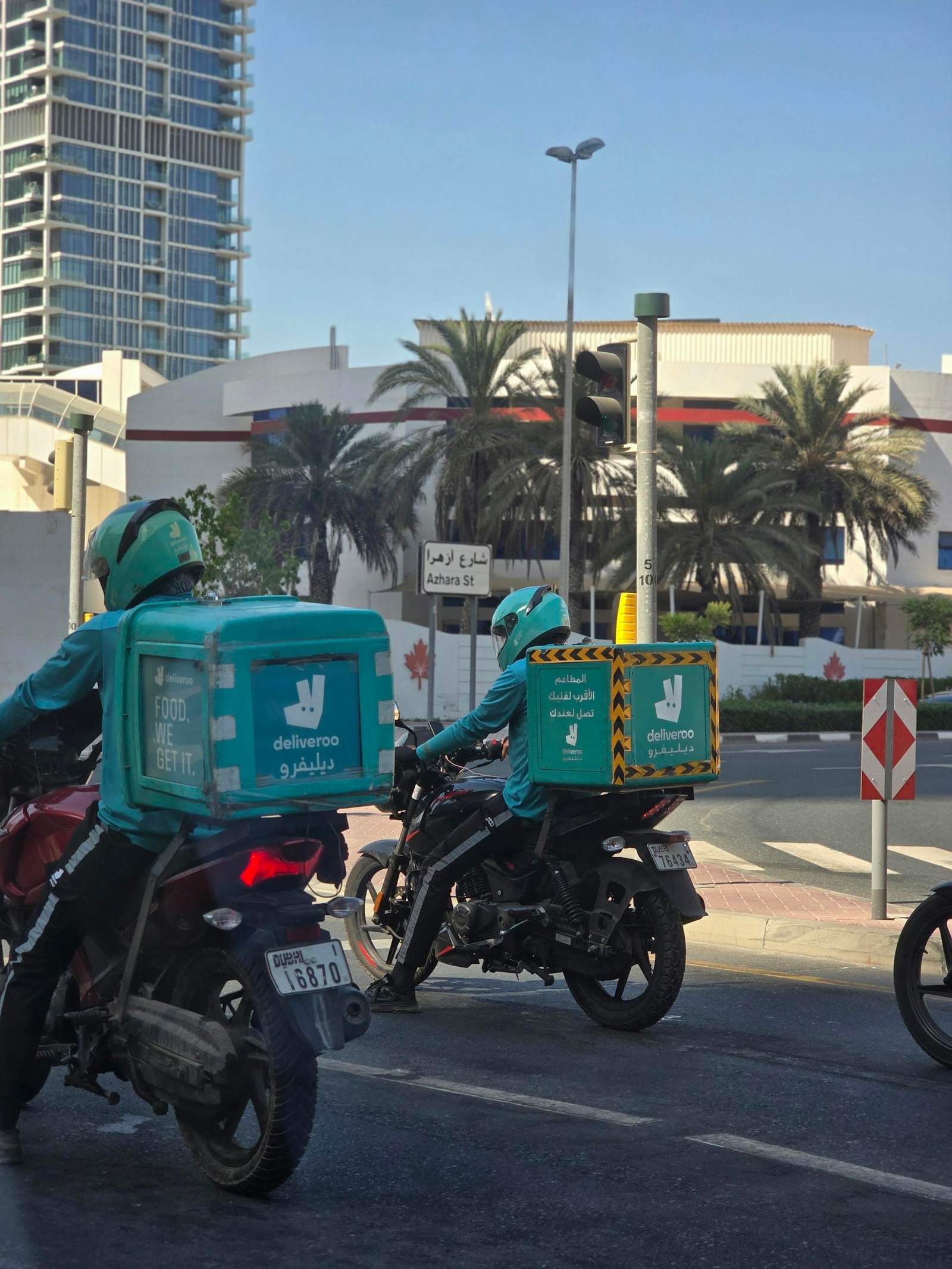 Deliveroo riders navigate Dubai streets with delivery boxes on motorbikes.