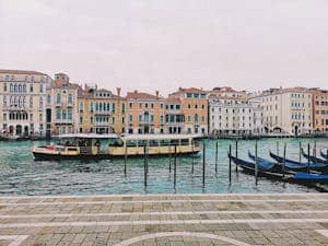 Picturesque view of Venice's canal with gondolas and a bustling ferry. Iconic architecture in the background.