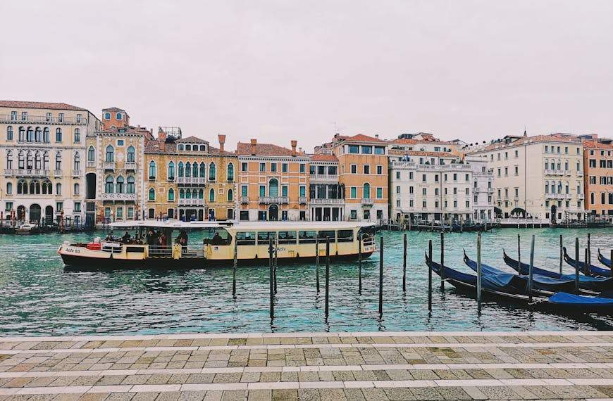 Picturesque view of Venice's canal with gondolas and a bustling ferry. Iconic architecture in the background.