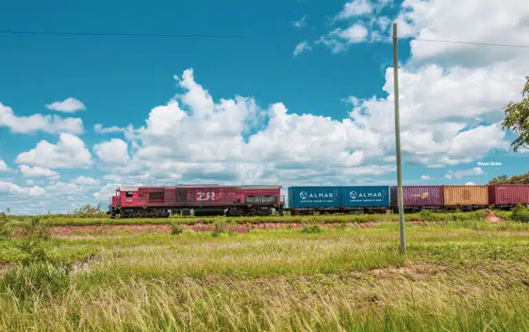 Freight train moving through the countryside under a blue sky.