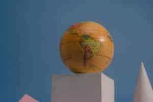 A vibrant globe on geometric shapes against a blue backdrop, showcasing continents and oceans.