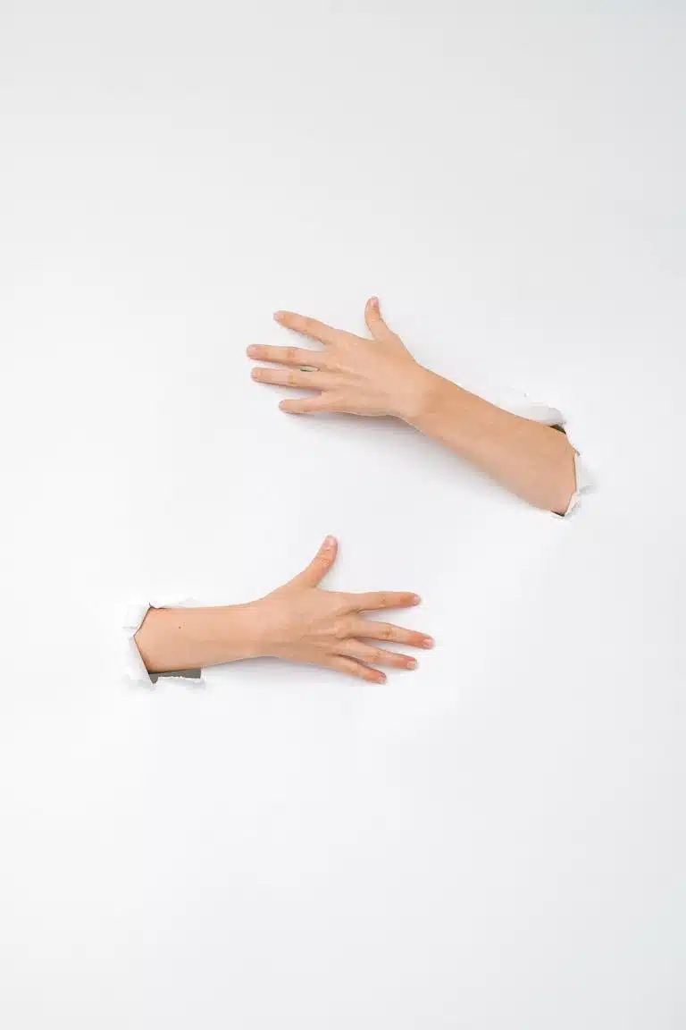 Two human hands reaching through holes in a white wall, symbolic of connection and exploration.