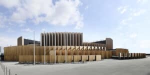 Circular wooden structure with tiered panels at Japan’s Expo 2025 Pavilion, featuring flags and a blue sky.